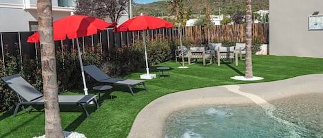A pool area with artificial grass, lounge chairs, and red umbrellas.