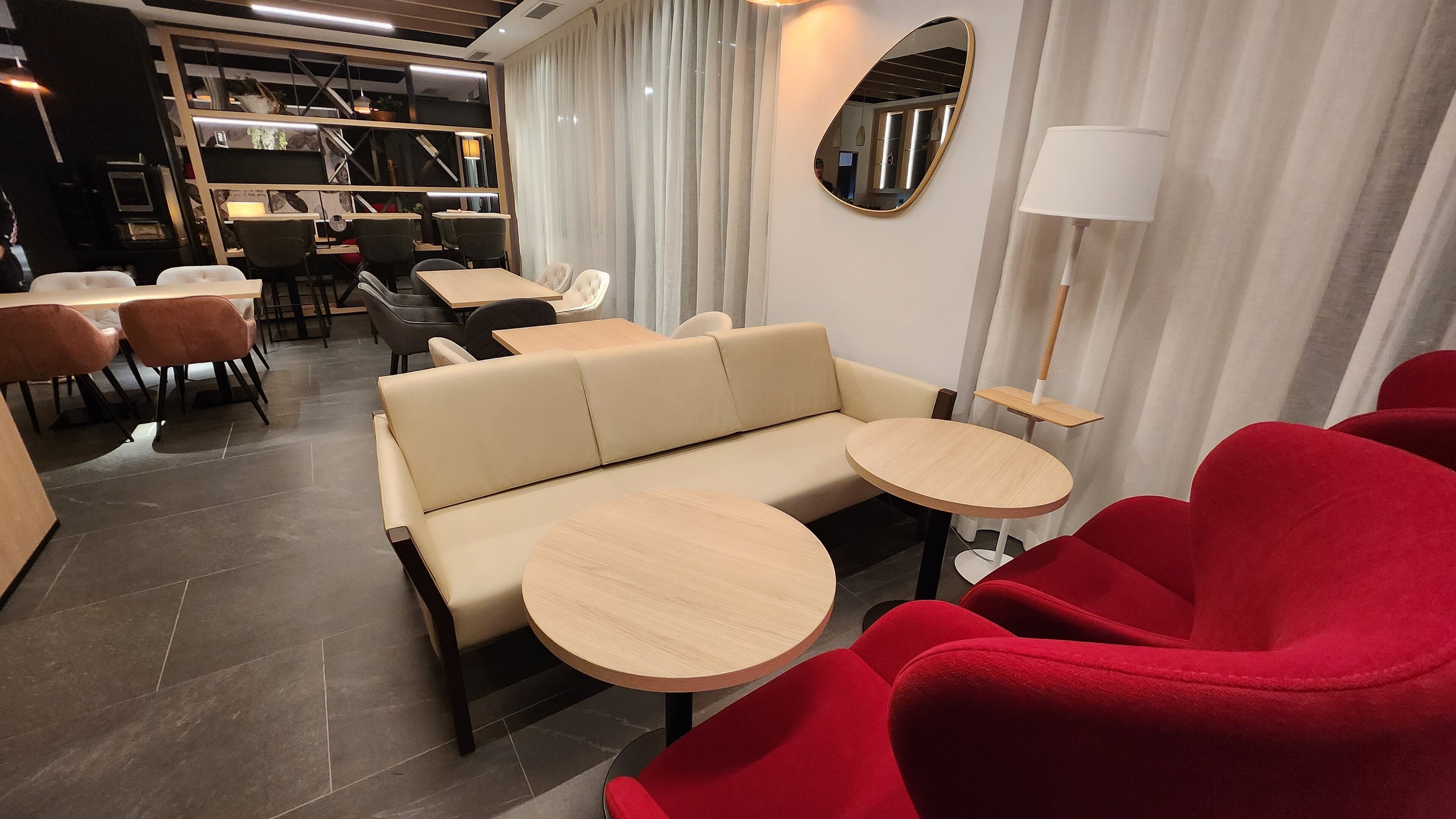 A modern lounge area with a sofa, red chairs, and round tables.
