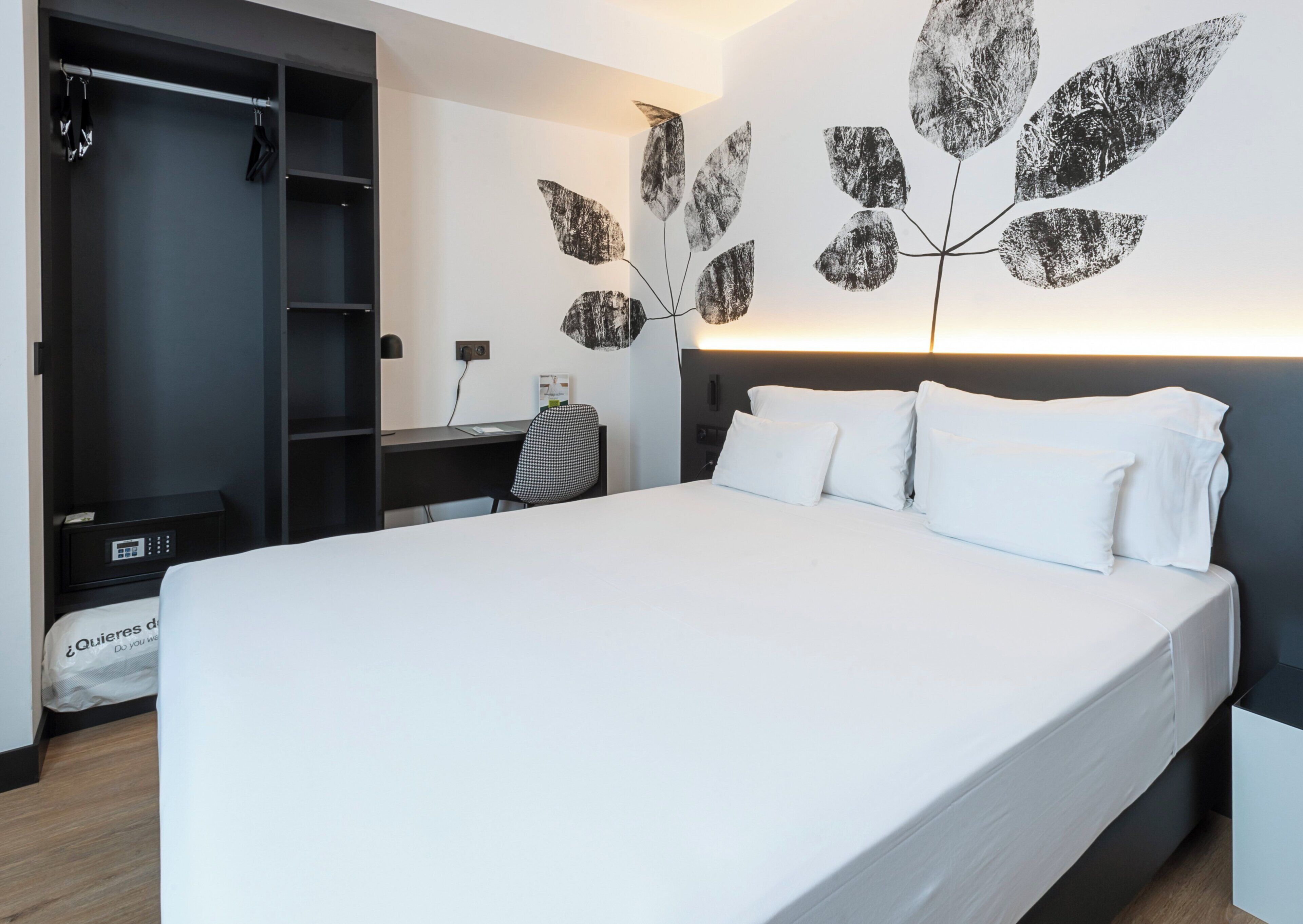 A modern hotel room with a large bed, a desk, and a wardrobe.
