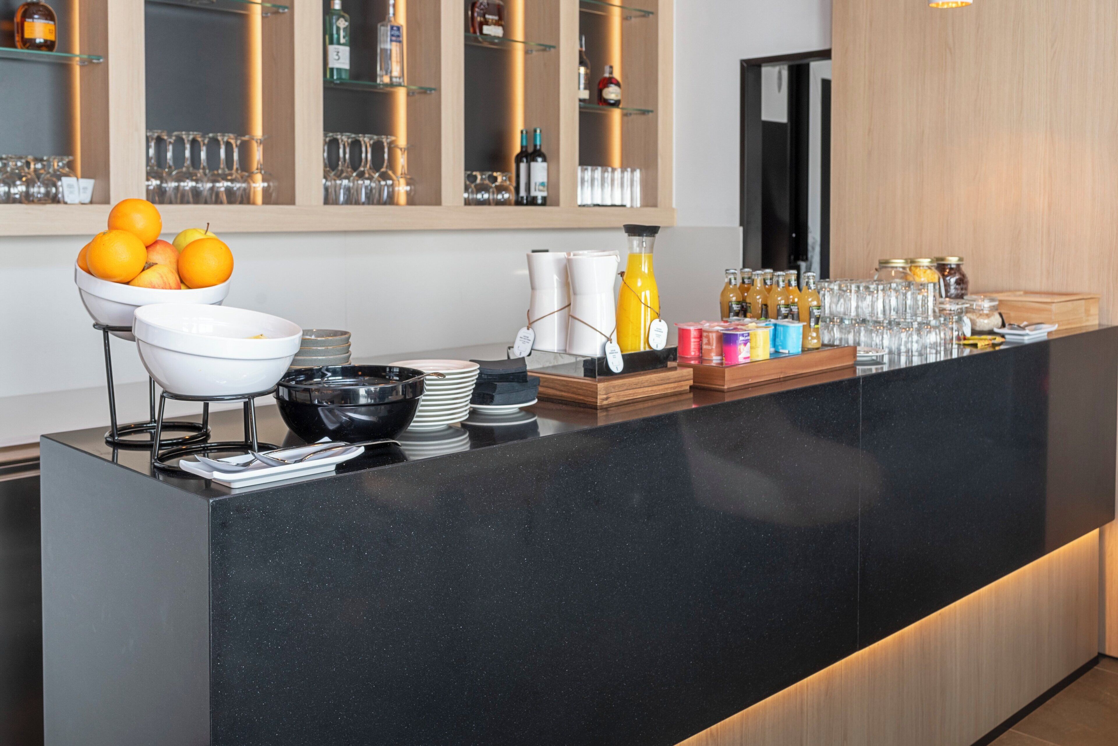 Een modern ontbijtbuffet met een zwarte toonbank, schalen met fruit en diverse ontbijtartikelen.
