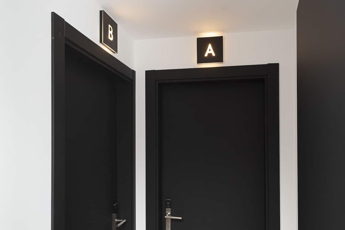 Um corredor com duas portas pretas, uma com a inscrição 'A' e outra com a inscrição 'B'.