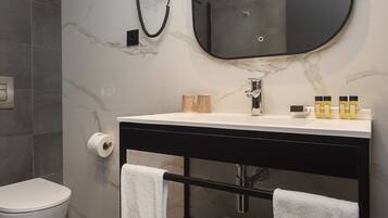 Un baño moderno con pared de mármol, tocador negro, un espejo grande y un inodoro.
