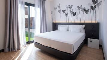 Une chambre d’hôtel moderne avec un grand lit, une table de chevet, un téléphone fixé au mur et une vue sur un balcon.