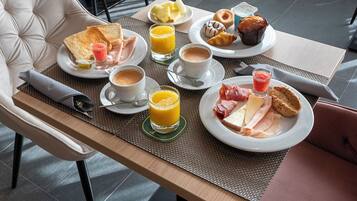 Una mesa de desayuno con tostadas, huevos, fruta, bollería y bebidas.