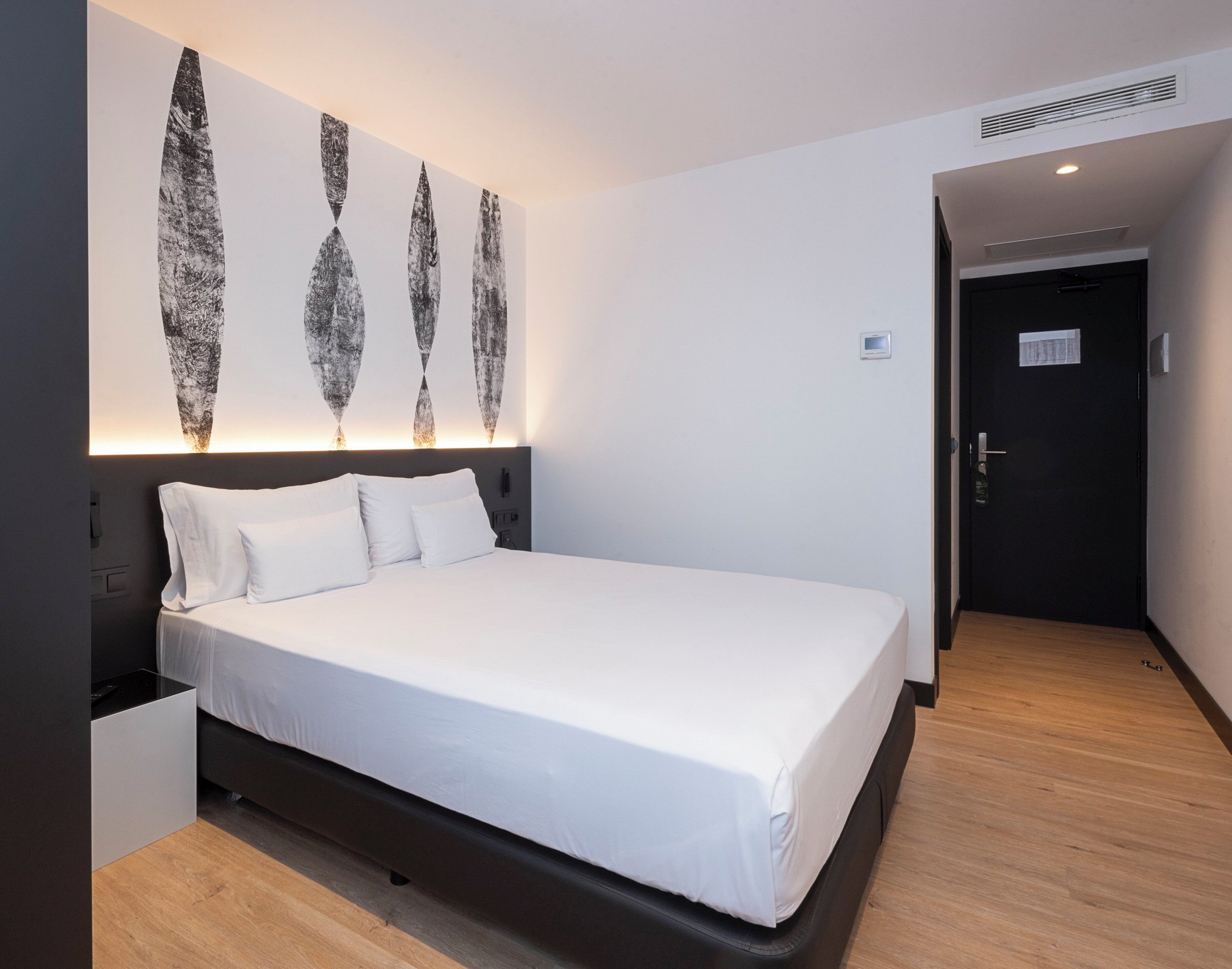 Een moderne hotelkamer met een groot bed, een hoofdbord met ingebouwde verlichting en een aan de muur hangend kunstwerk.