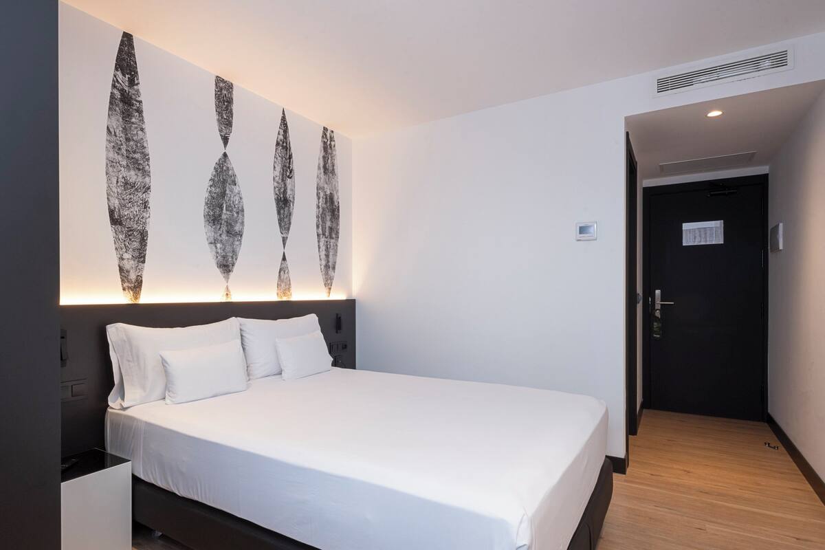 Una habitación de hotel moderna con una cama grande, cabecera con iluminación integrada y una obra de arte colgada en la pared.