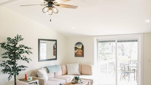 Un salon spacieux doté d’un ventilateur de plafond, d’un canapé, d’une table basse et d’une grande fenêtre offrant une vue sur l’extérieur.