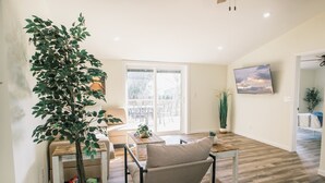 Un salon spacieux avec une grande fenêtre, un canapé, une table basse et un téléviseur fixé au mur.