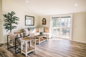 Een ruime woonkamer met een grote bank, twee bijzettafels en een potplant.