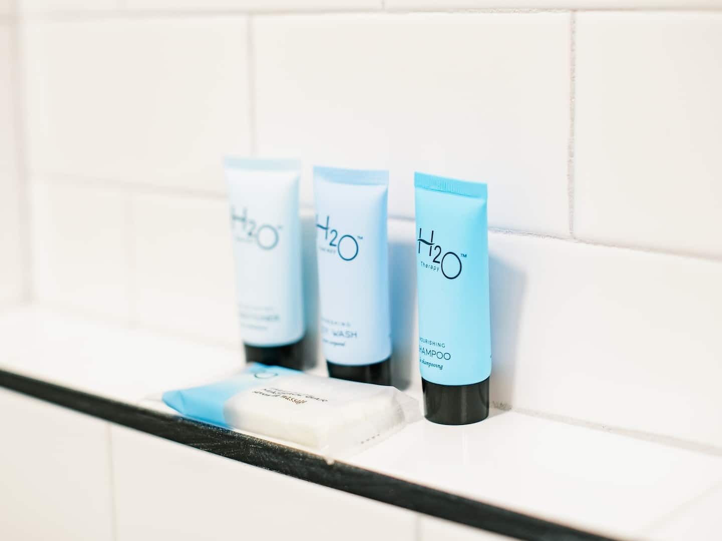 Trois bouteilles de shampooing H2O Therapy sur une étagère carrelée de carreaux blancs.