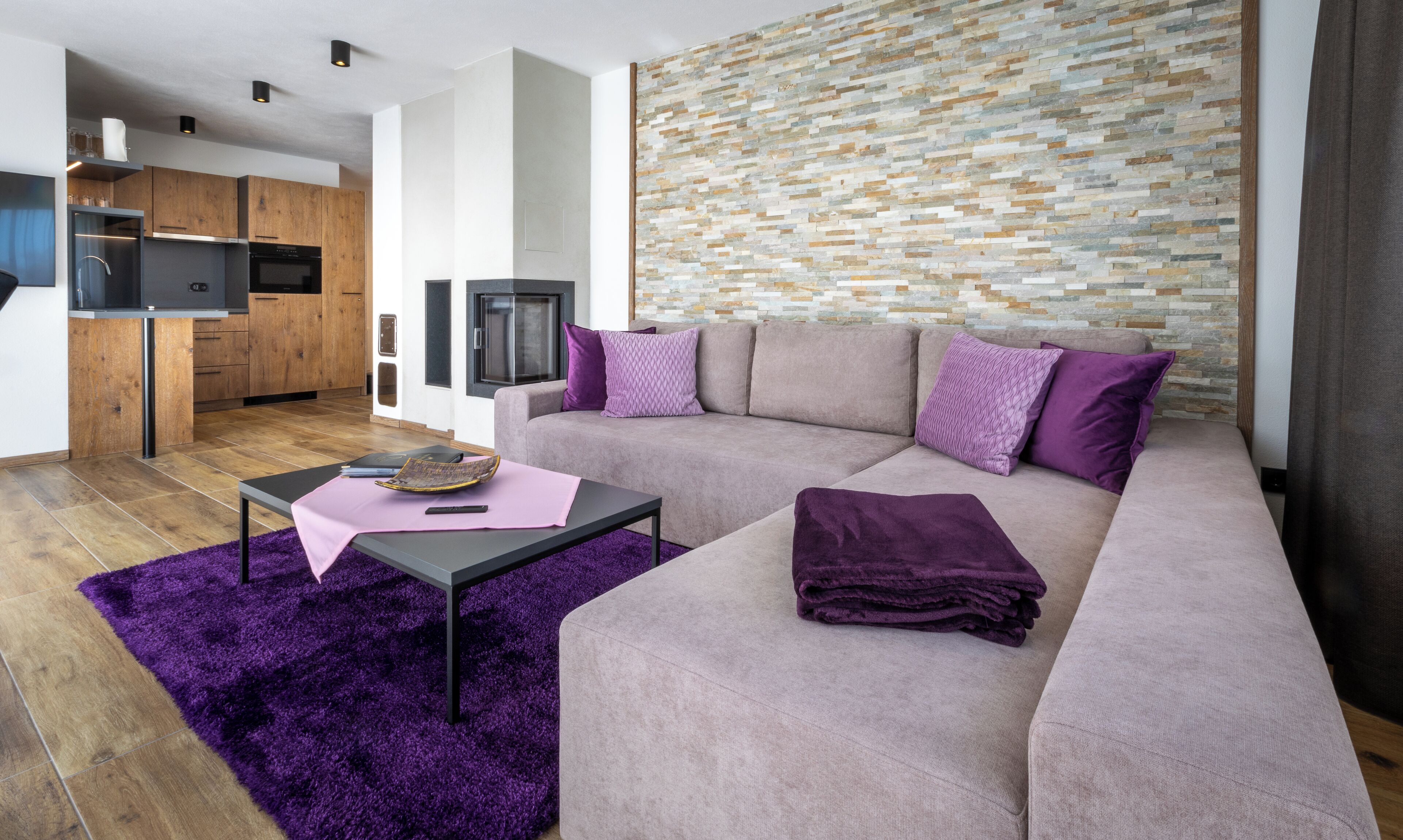Un salon moderne avec un canapé d’angle, une table basse et un tapis violet.