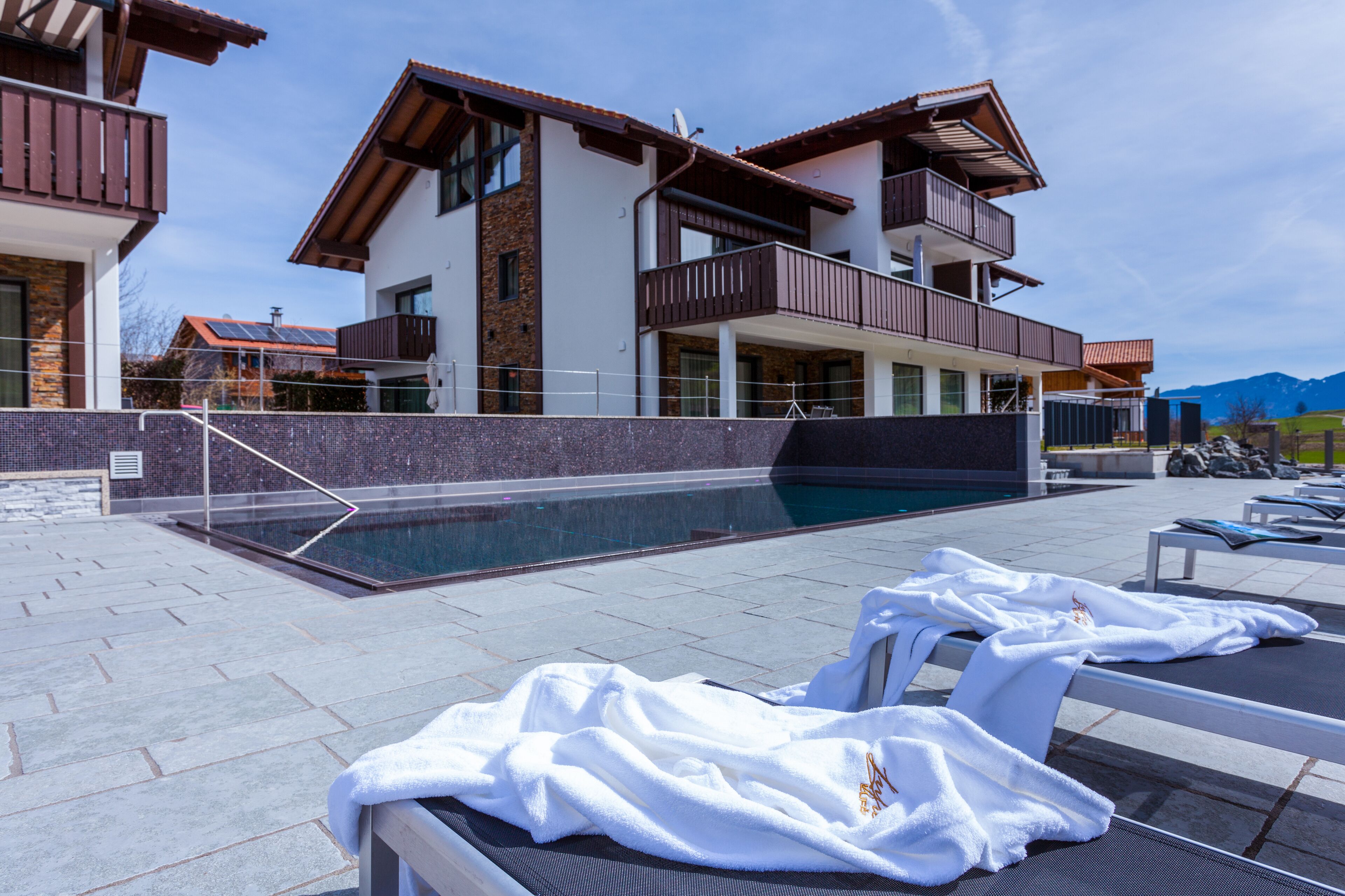 A modern building with a swimming pool, lounge chairs, and towels.