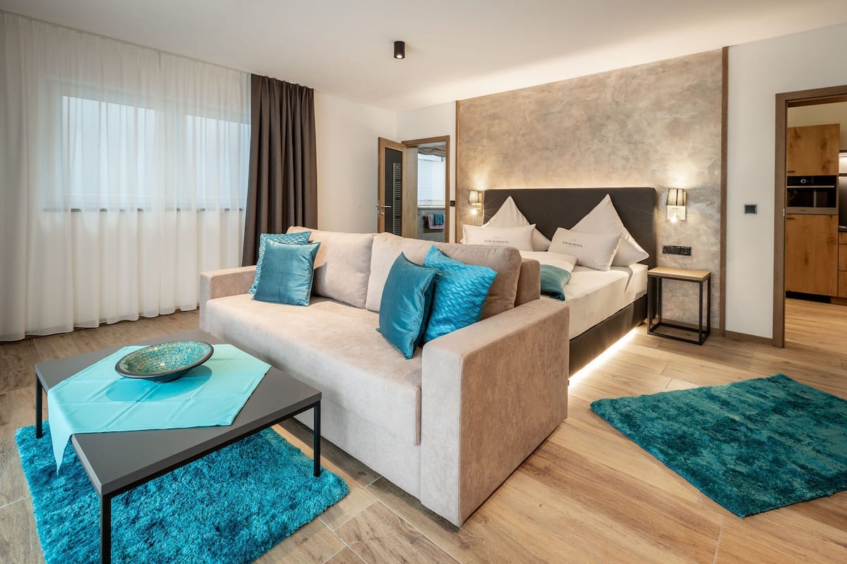 A modern hotel room with a sofa, a bed, a small table, and a nightstand.