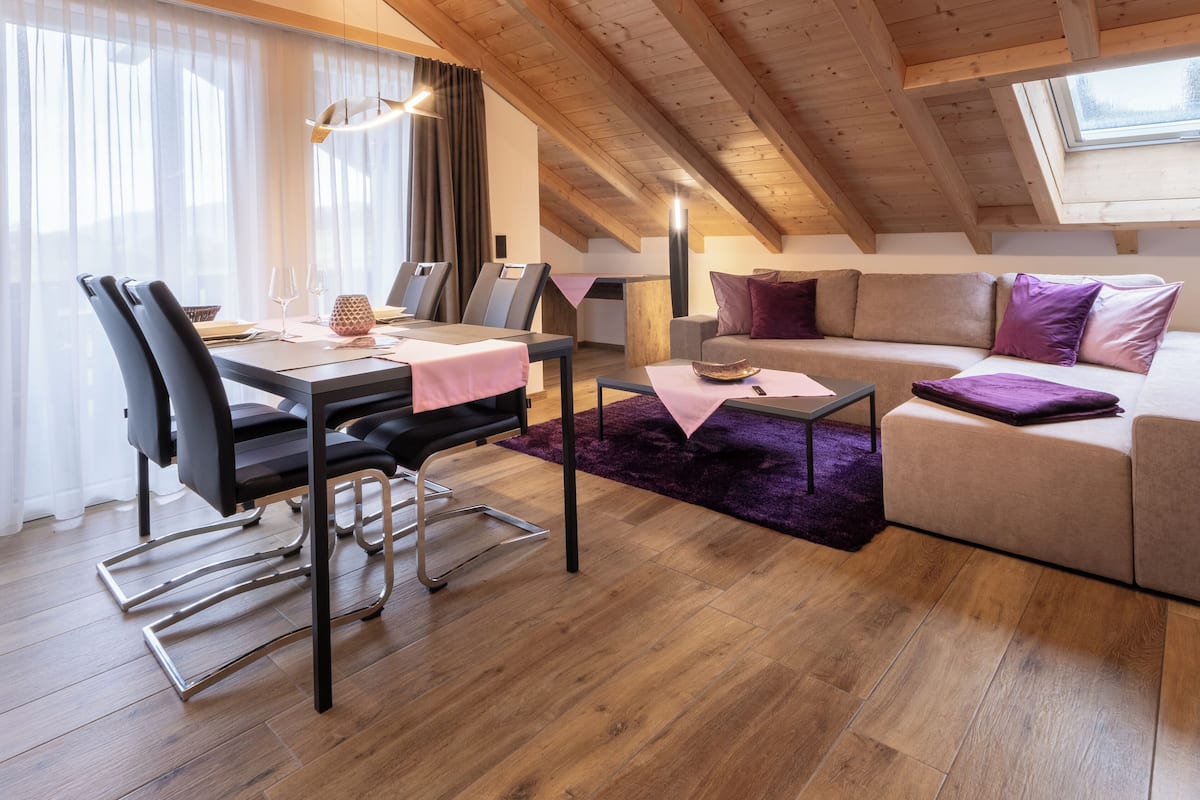 A cozy loft-style room with a dining area, a sofa, and a window with a view.