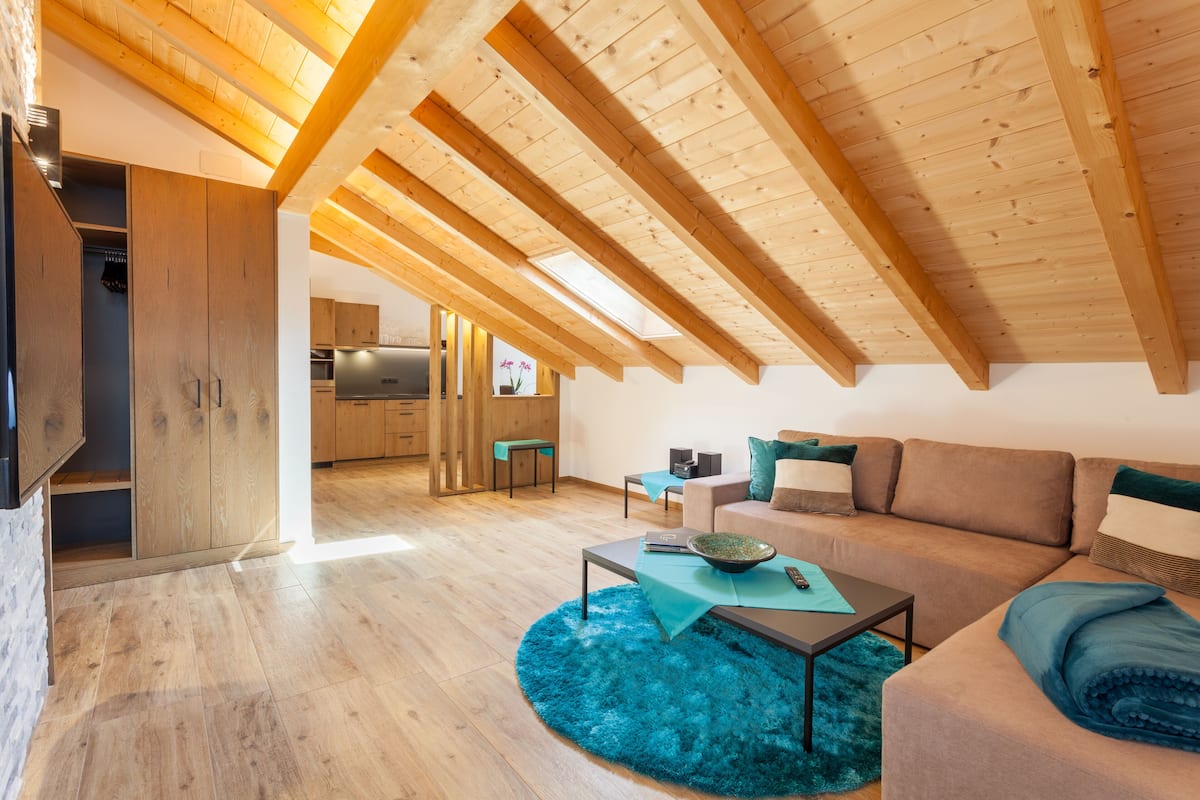 A modern loft with exposed wooden beams, a cozy living area with a sofa and coffee table, and a kitchen in the background.