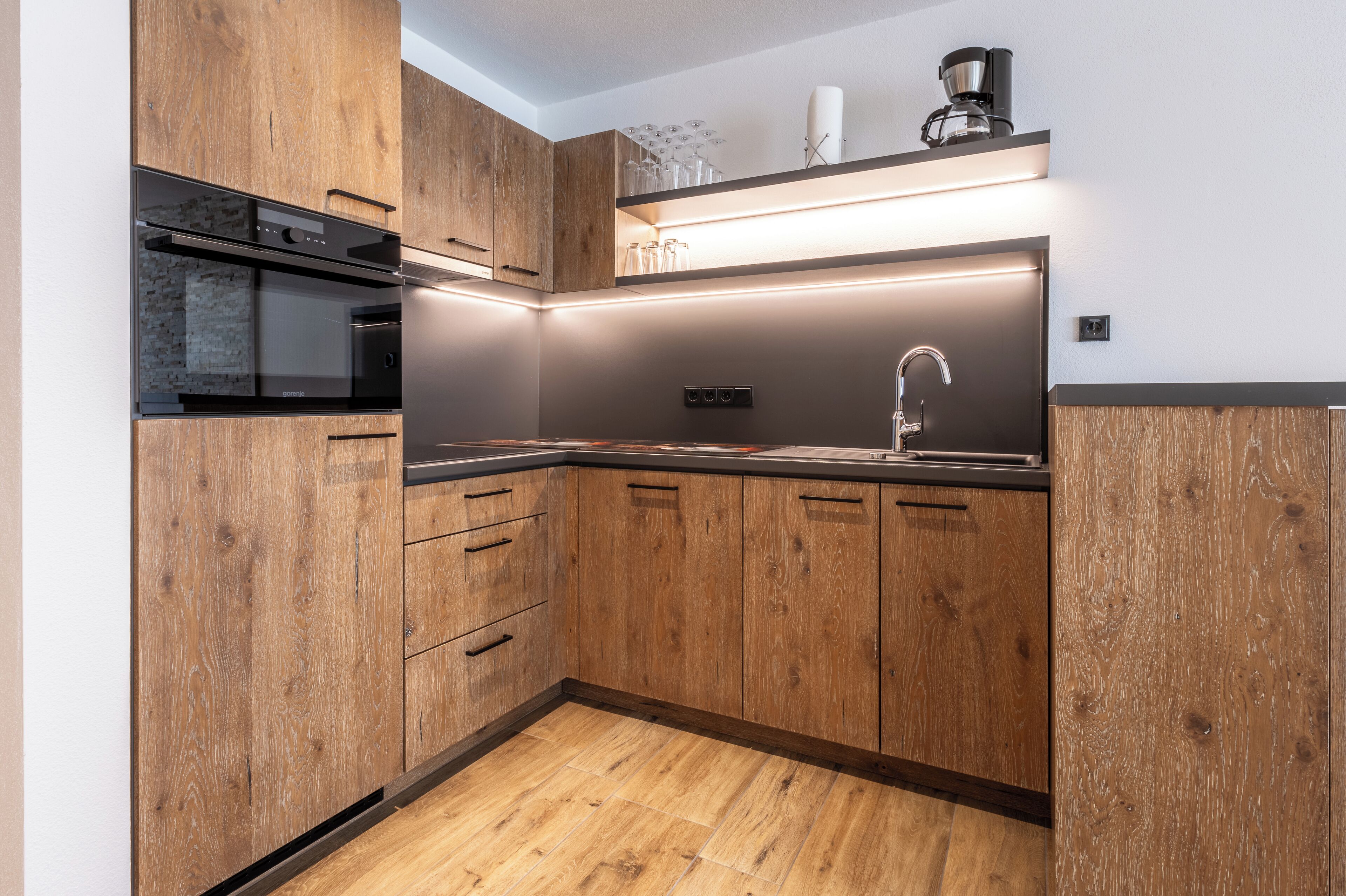 A modern kitchen with wooden cabinets, a built-in oven, and a stainless steel sink.
