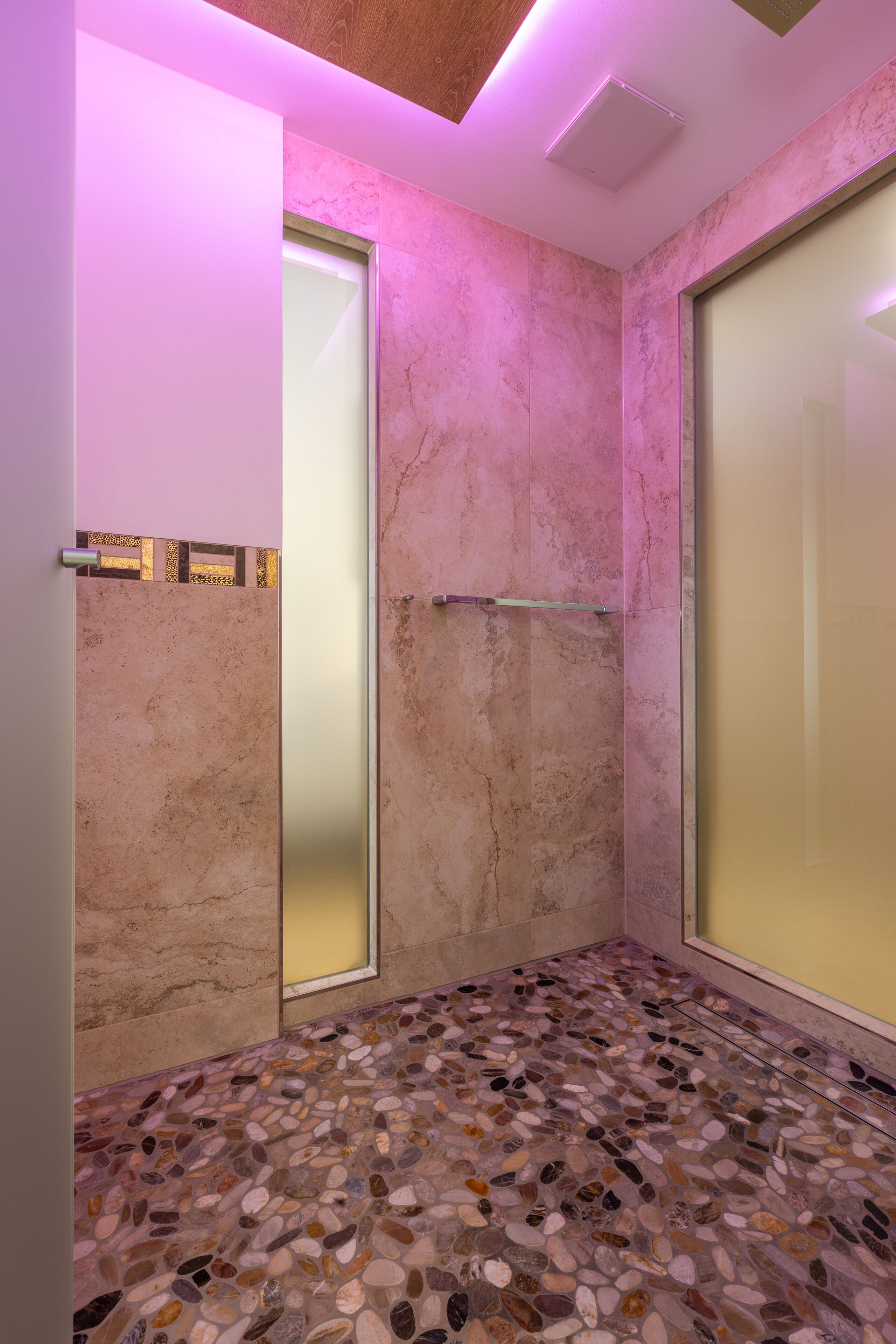 Ein modernes Badezimmer mit einem fußbodenähnlichen Kieselmuster, Milchglasüren und rosafarbenem Ambiente-Licht.