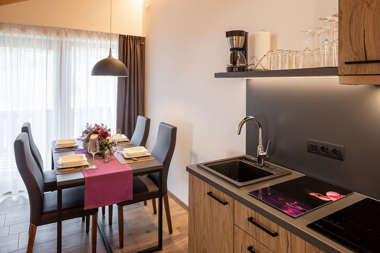 Une cuisine moderne avec un coin repas, comprenant une cuisinière encastrée, un évier et une machine à café posée sur une étagère.