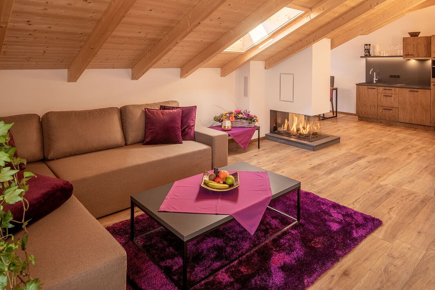 Un salon chaleureux avec un plafond en bois, un canapé, une table basse sur laquelle sont disposés des fruits et une cheminée.