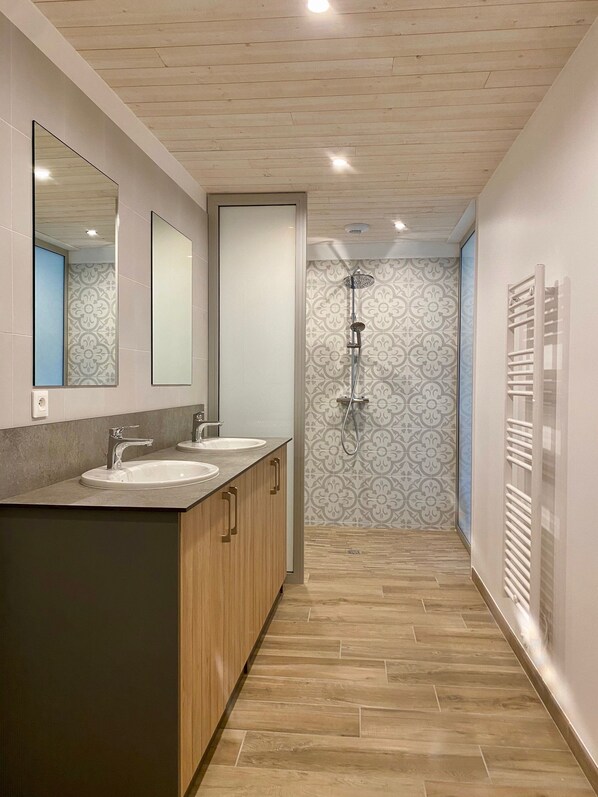 Uma casa de banho moderna com duas pias, chuveiro e porta-toalhas.