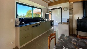 A modern kitchen with a large window, built-in appliances, and a stone fireplace. - Gîte 12/14 pers. in the countryside 10km from Barfleur and Saint-Vaast-la-Hougue (Teurthéville-Bocage)