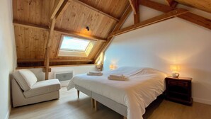 A bedroom with a sloped ceiling, a skylight, a bed, a nightstand, a chair, and a bedside table. - Gîte 12/14 pers. in the countryside 10km from Barfleur and Saint-Vaast-la-Hougue (Teurthéville-Bocage)