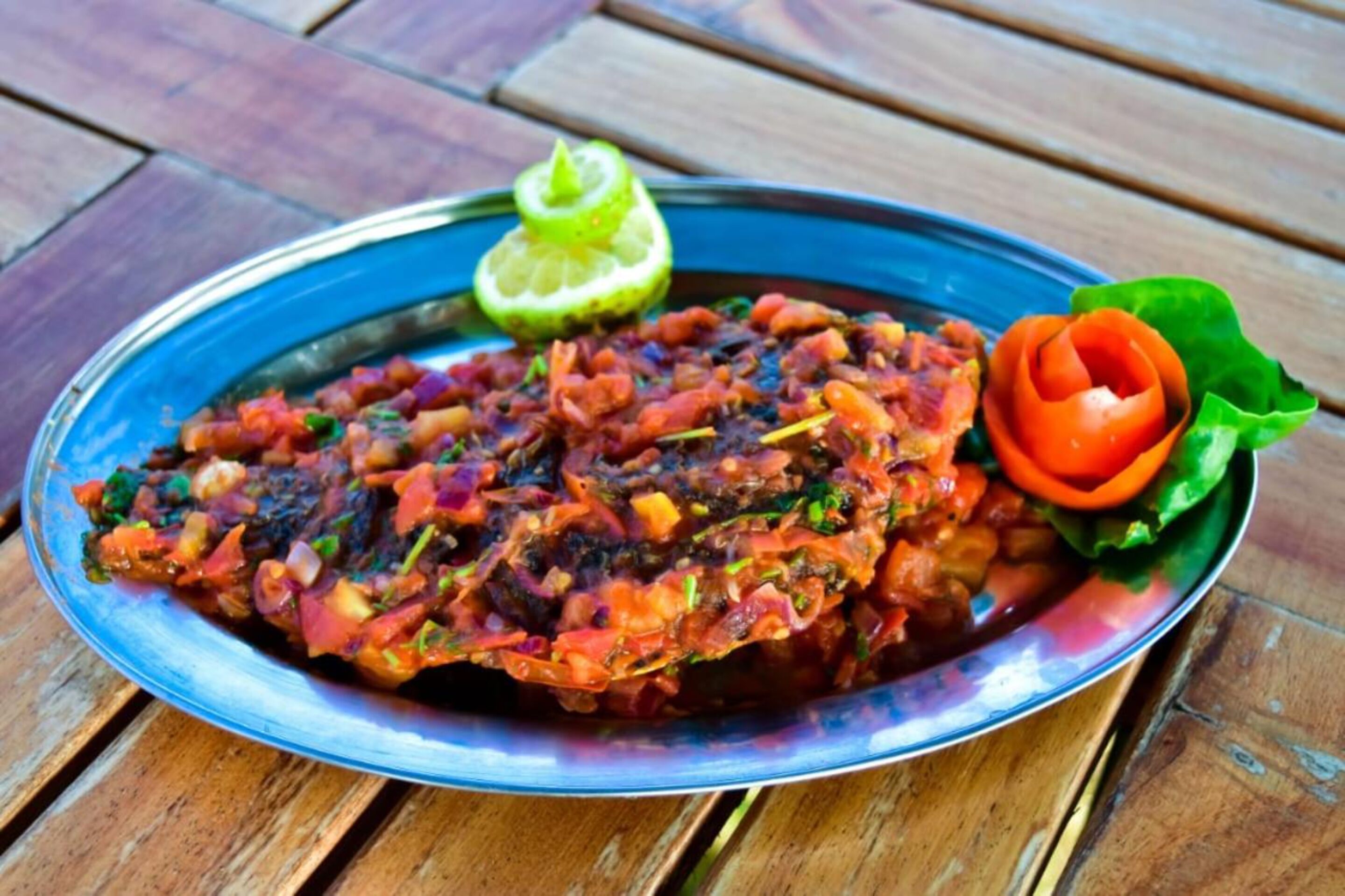 A plate of food with a lime wedge and a decorative leaf on a wooden table.