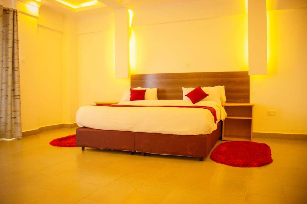 A modern hotel room with a large bed, a wooden headboard, and a red rug.
