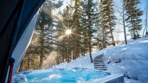 Un bain à remous dans une forêt enneigée, avec un escalier en bois menant à un niveau supérieur.