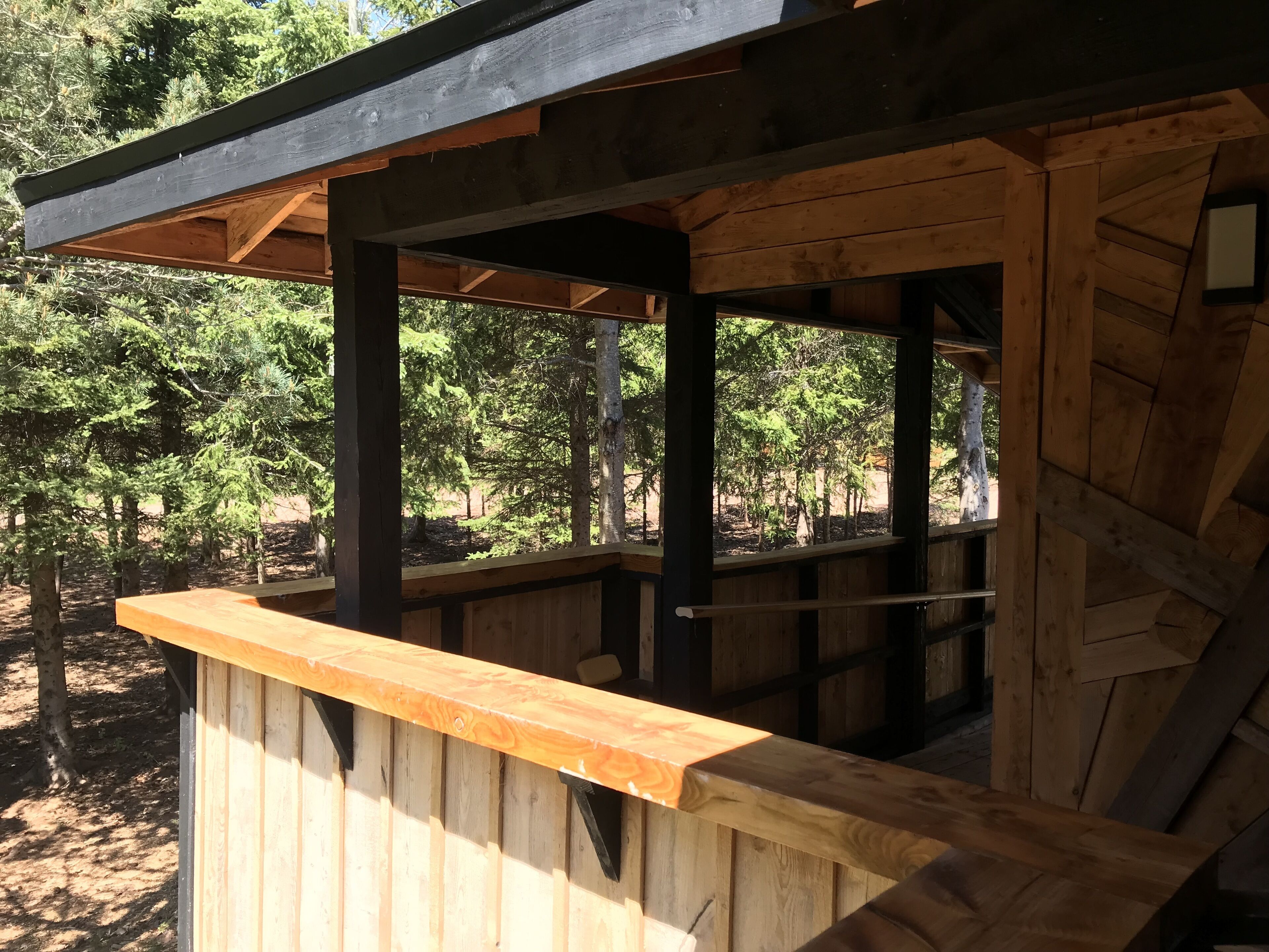 A wooden structure with a bench and a covered area, surrounded by trees.
