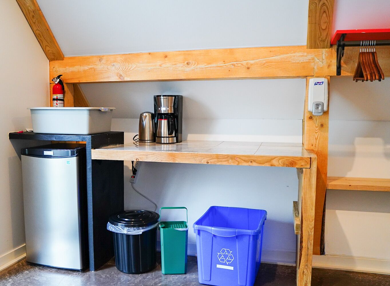 A compact kitchenette with a coffee maker, trash bins, and a recycling bin.