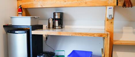 A compact kitchenette with a coffee maker, trash bins, and a recycling bin.