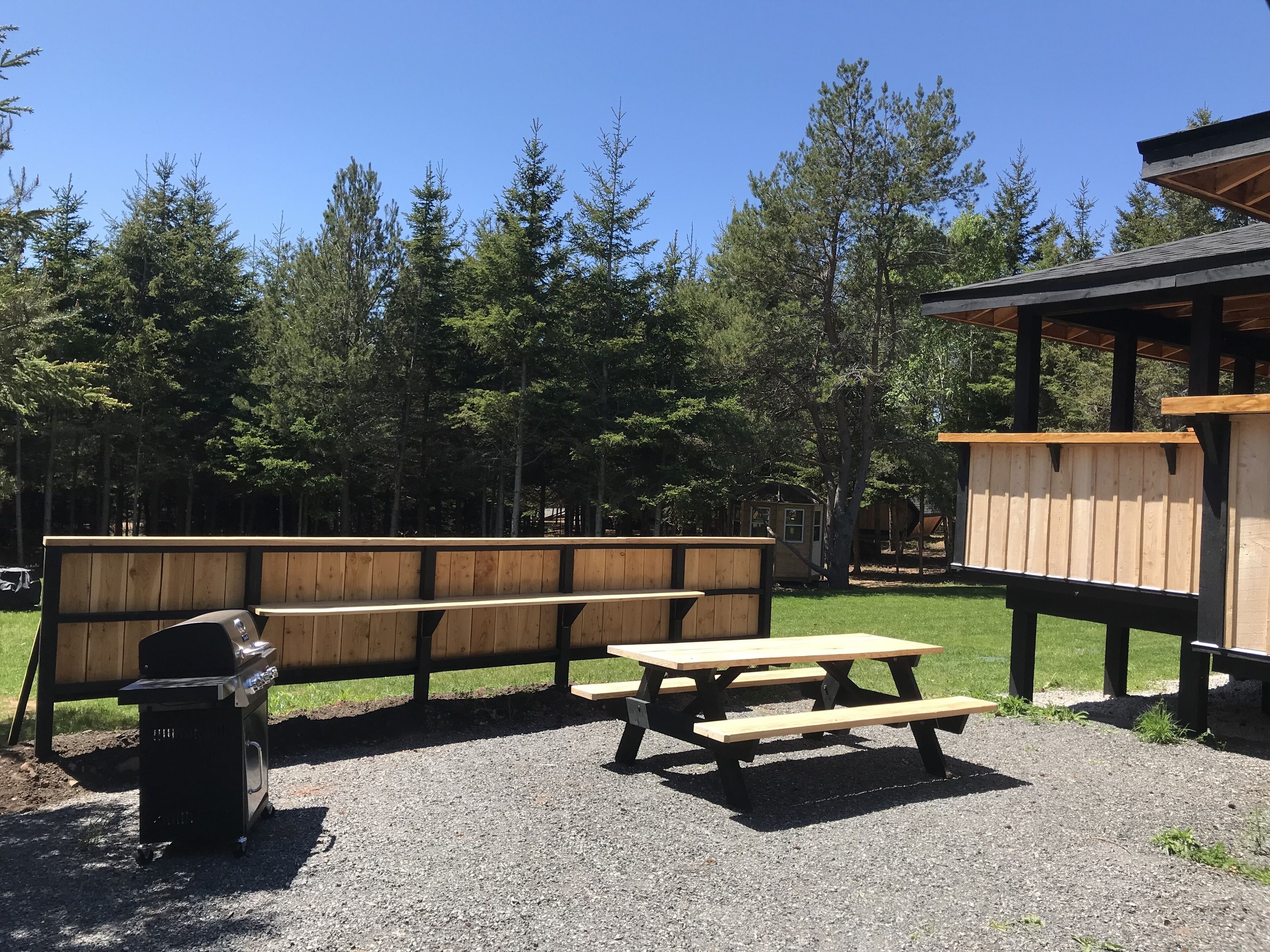 Un espace pique-nique équipé de bancs et d’un barbecue, entouré d’arbres.
