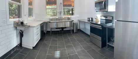 Una cocina moderna con electrodomésticos de acero inoxidable, un lavamanos grande y una ventana con vistas a la vegetación.