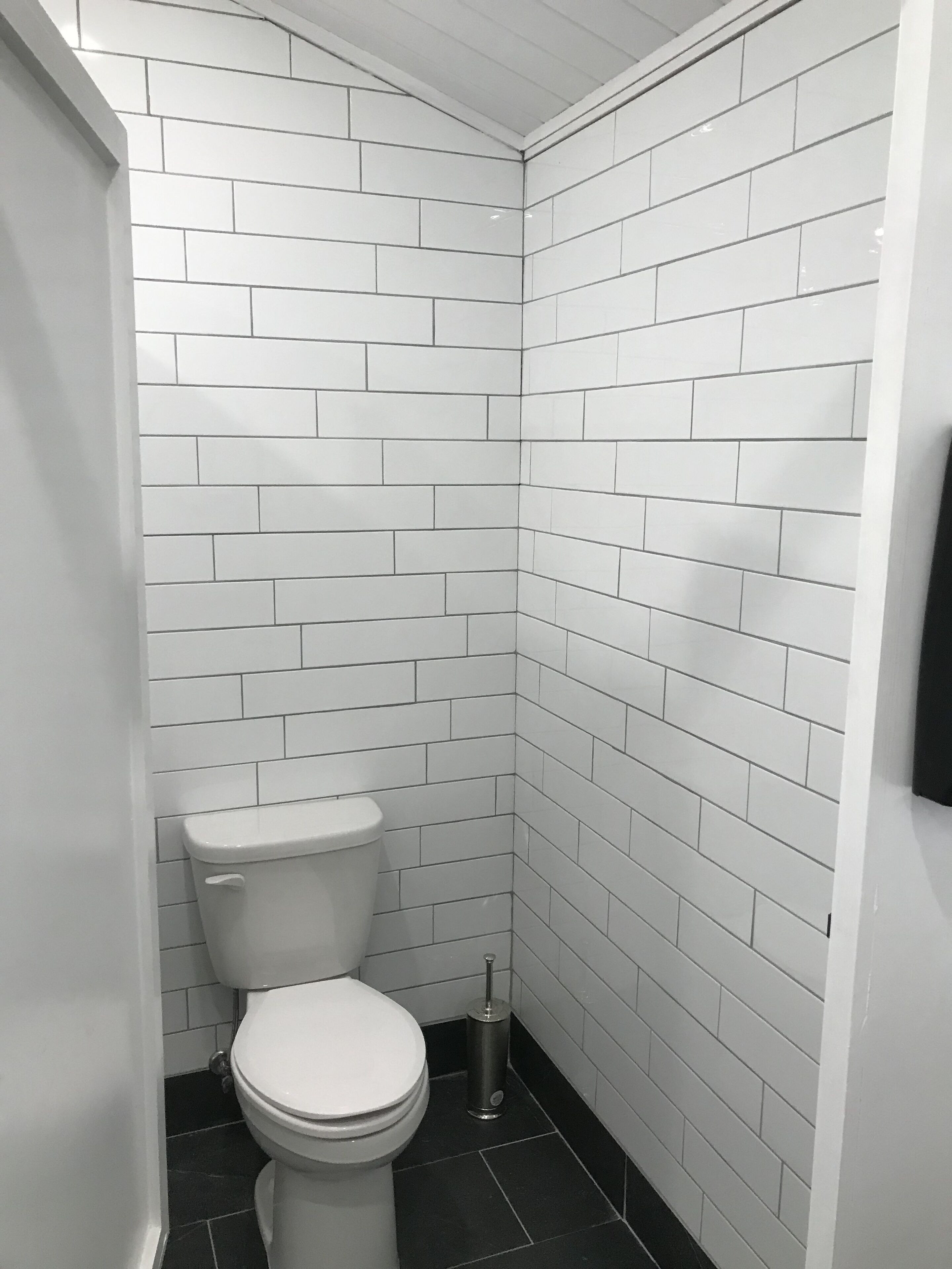 Un baño con azulejos blancos tipo metro en las paredes y un inodoro blanco.
