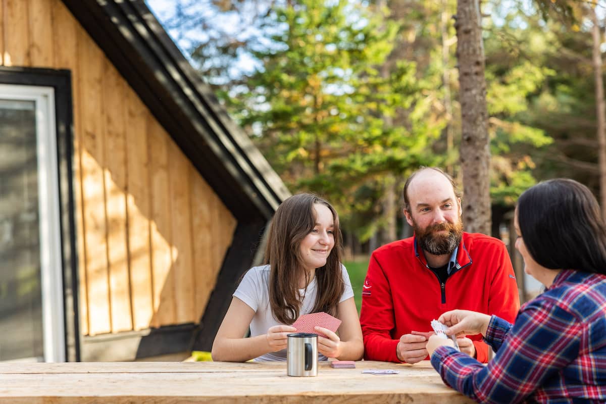 Uma cabana de madeira com uma janela grande e uma mesa onde pessoas jogam cartas.