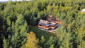 Un chalet à deux étages, entouré d’une forêt dense, doté d’une terrasse et d’un espace extérieur couvert.