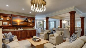 A spacious living room with a large TV, comfortable seating, wooden cabinets, and a chandelier.