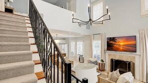 A spacious living area with a staircase, a fireplace, and a large TV displaying a sunset scene.