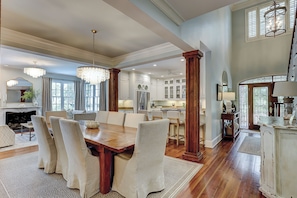 A spacious dining area with a wooden table and chairs, a chandelier, and a view of the kitchen and living room. - 20 Canvasback: Beautiful Compound w/ Pool, 4th row (3 min walk) to the Ocean (Hilton Head Island)
