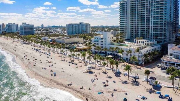 A beach with palm trees, a hotel, and high-rise buildings in the background. - Cozy - full kitchen & 10ft island - 1.2G Wifi (Fort Lauderdale)