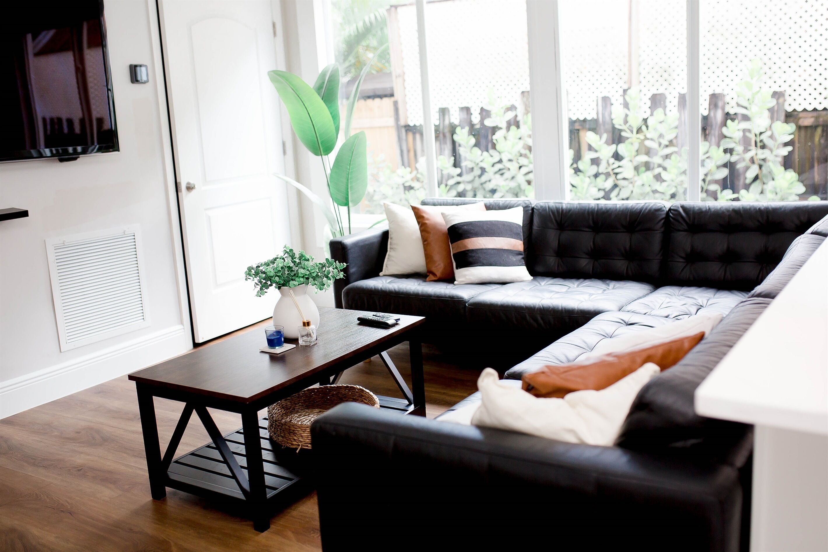 Un salón moderno con un sofá de cuero negro, una mesa de centro de madera y un ventanal con vistas a zonas verdes.