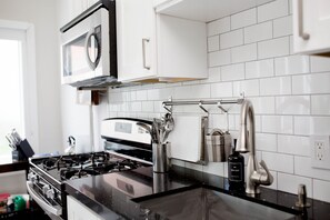 Une cuisine moderne avec un plan de travail noir, des appareils en acier inoxydable et un dosseret de carrelage blanc.