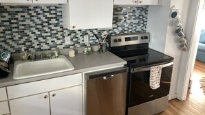 Eine kompakte Küche mit weißen Schränken, einem Edelstahl-Geschirrspüler und einem schwarzen Backofen.