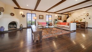 A spacious living room with a fireplace, wooden beams, and a large window. - Stunning Spanish Pool Home (Glendale)