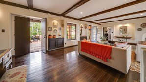 A spacious living room with hardwood flooring, a white sofa with a red throw, and a dining area visible through an open door. - Stunning Spanish Pool Home (Glendale)