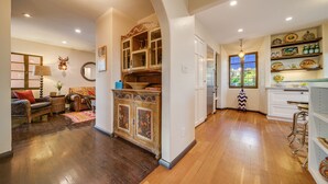 A spacious living area with a wooden floor, a sofa, a dining table, and a kitchen area with white cabinets and shelves. - Stunning Spanish Pool Home (Glendale)