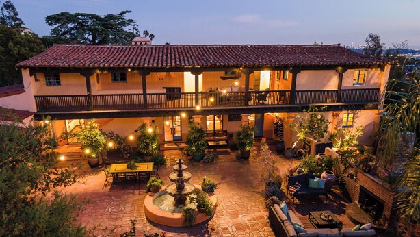 A two-story building with a courtyard featuring outdoor seating, a fountain, and a fire pit. - Stunning Spanish Pool Home (Glendale)
