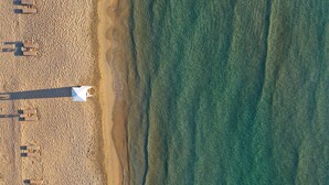Vista aérea de una playa con varias tumbonas y una estructura blanca, posiblemente una torre de salvavidas, cerca de la orilla.