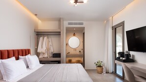 Una habitación de hotel moderna con una cama grande, un escritorio con televisor de pantalla plana, un vestidor, un espejo redondo y un ventanal amplio.